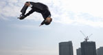 A businessman does a somersault in the air against a background of skyscrapers.