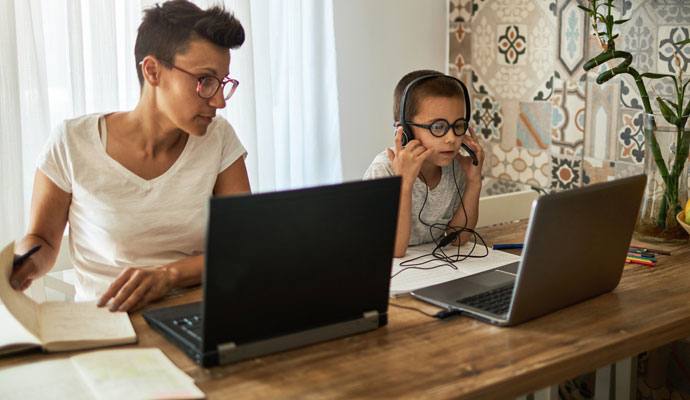 A boy attends virtual school while his mother works from home beside him