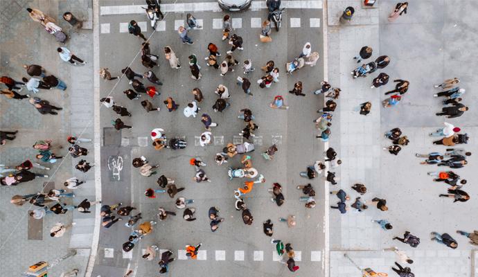 An overhead city view shows a crowd of people crossing an intersection from all directions.