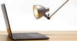 Bent-arm desk lamp is angled to shine directly into the screen of a laptop