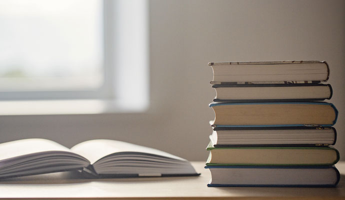 A photograph of a stack of six books on a table; an open book is to the left of the stack. A photograph of a stack of six books on a table; an open book is to the left of the stack.