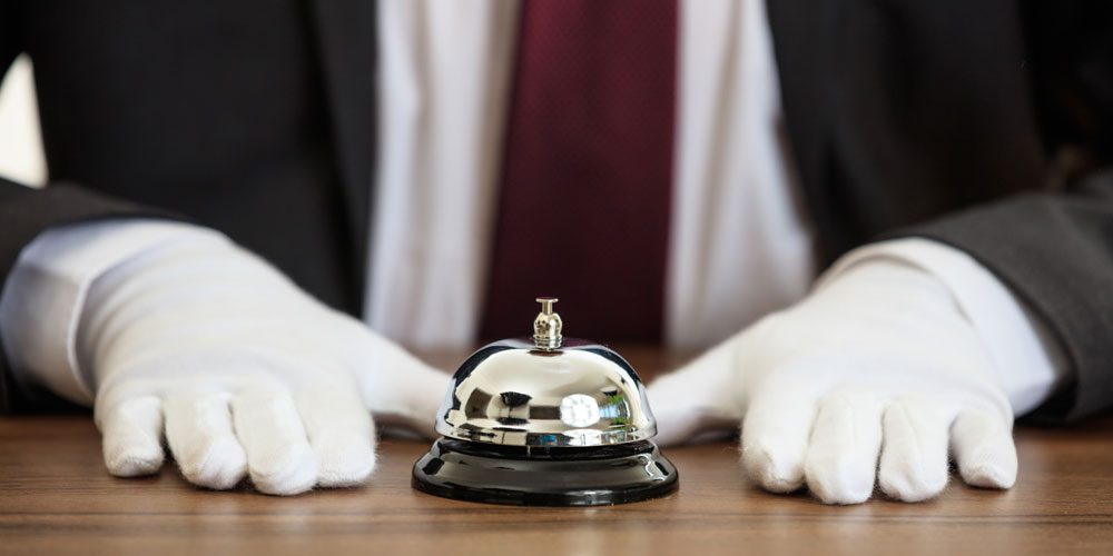 A butler’s hands rest on either side of a service bell.