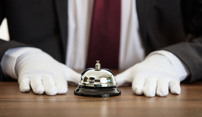 A butler’s hands rest on either side of a service bell.