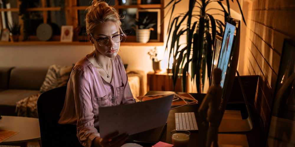 A businesswoman seated in a home office works into the evening. A businesswoman seated in a home office works into the evening.