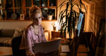 A businesswoman seated in a home office works into the evening.