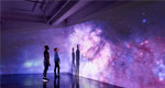 An image of two people looking at a large scale projected image of space.