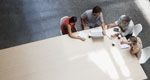An overhead view shows a team of businesspeople meeting at a conference table.