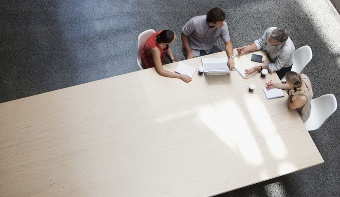 An overhead view shows a team of businesspeople meeting at a conference table.