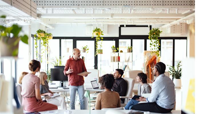 A small team of coworkers in casual dress meets in a bright, open workspace.