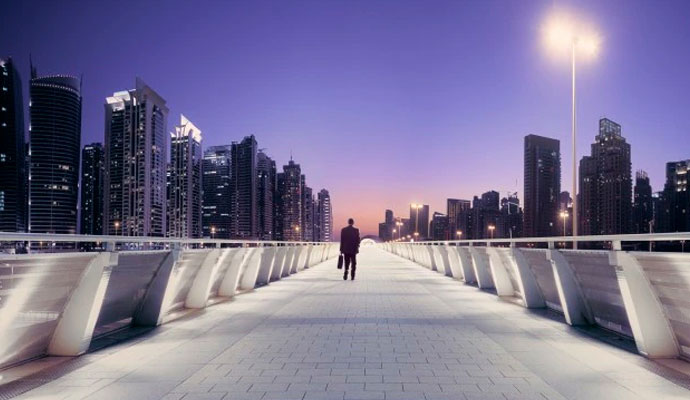 A photograph of a business executive walking along a bridge with a city skyline in the background.