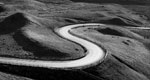 A black-and-white photo of an empty, curving road with hills.
