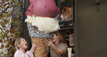 Photograph of a girl being handed a gigantic ice cream cone.