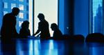 Four executives in silhouette talk at end of conference table.