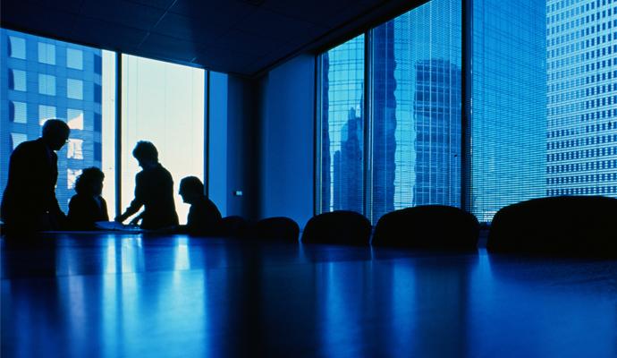 Four executives in silhouette talk at end of conference table.