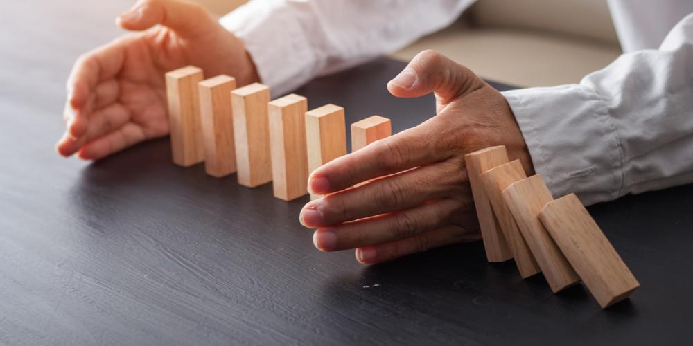A man places his hands around a section of dominos, shielding them from a line of cascading pieces.