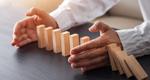 A man places his hands around a section of dominos, shielding them from a line of cascading pieces.