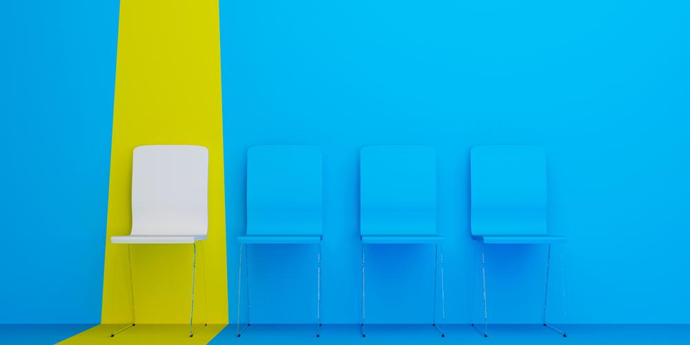 In a row of blue chairs set against a blue background, a white chair is highlighted by a bright, yellow stripe.  In a row of blue chairs set against a blue background, a white chair is highlighted by a bright, yellow stripe.