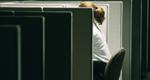 Photograph of a woman, partially hidden by a cubicle partition, alone in an empty office.