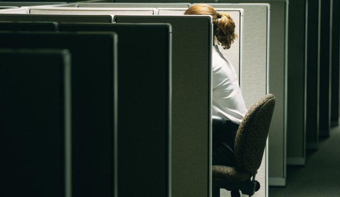 Photograph of a woman, partially hidden by a cubicle partition, alone in an empty office.
