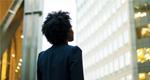 A photograph of a woman in business clothes looking up at an office building.