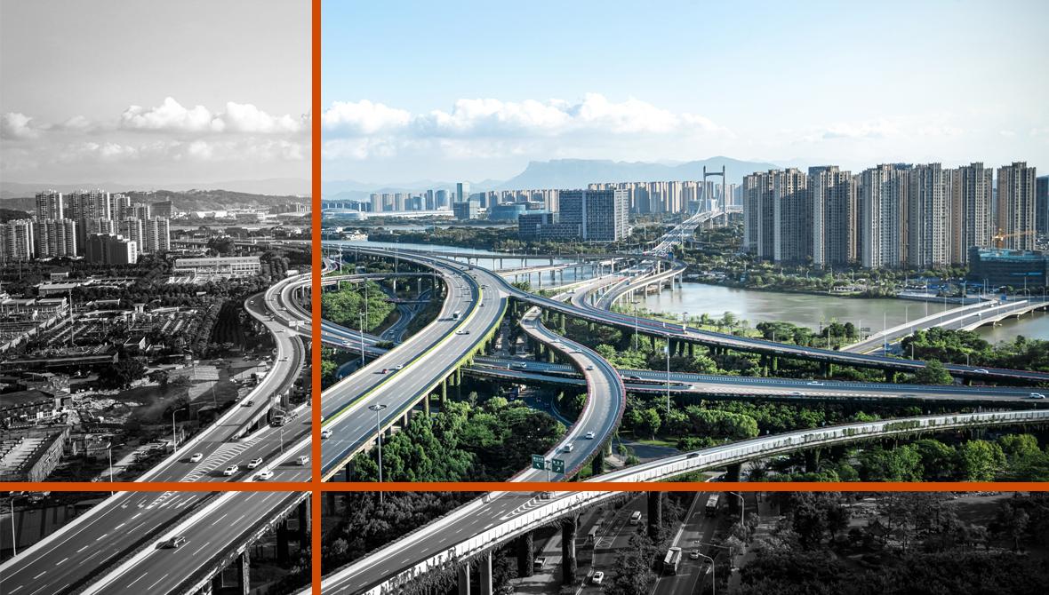 Elevated highways pass above trees and cross a river, en route to a city skyline. A mountain range rises in the far distance.