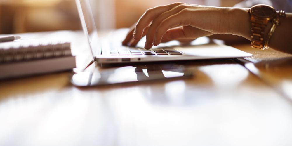 A pair of hands types on a laptop in a cafe setting A pair of hands types on a laptop in a cafe setting