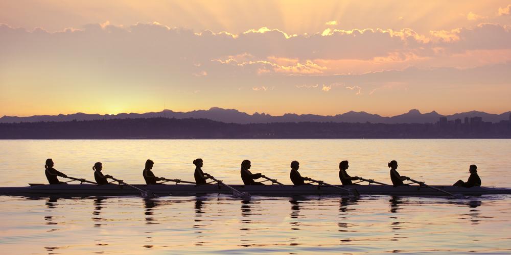 A photograph of a rowing team on the water at sunrise 