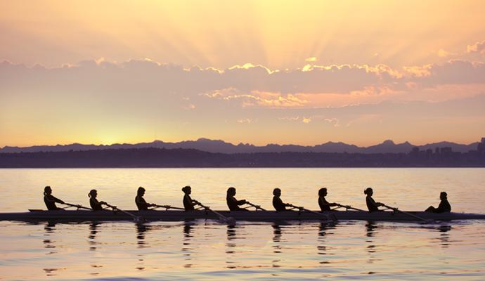 A photograph of a rowing team on the water at sunrise 