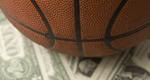 A close-up photo of a basketball sitting on dollar bills