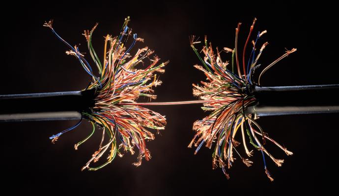 A photograph of a severely frayed electrical cable against a black background.