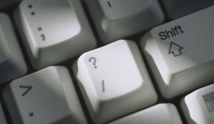 A close-up view of a computer keyboard focuses on the question-mark key