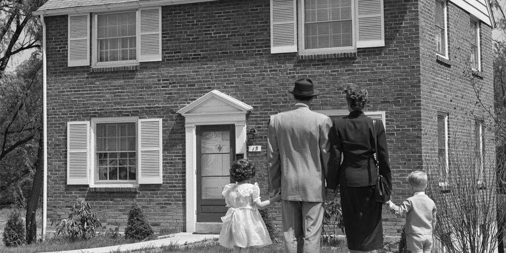 A well-dressed family of four standing in front of a suburban house around 1950