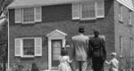 A well-dressed family of four standing in front of a suburban house around 1950