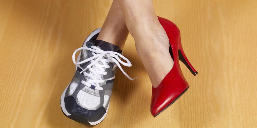 A woman’s crossed legs show a sneaker on one foot and a dress shoe on the other