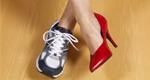 A woman’s crossed legs show a sneaker on one foot and a dress shoe on the other