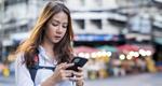 A photograph of a young woman gazing into her smartphone on a city street.