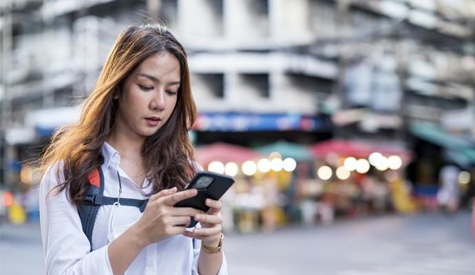 A photograph of a young woman gazing into her smartphone on a city street.