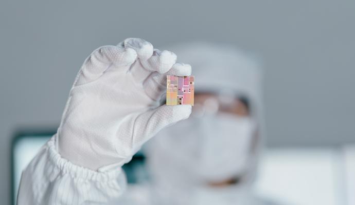 A photograph of a chip engineer in a clean-room suit holding up a chip