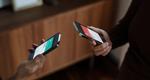 A cropped image shows the hands of two people holding smartphones, which they use to transfer funds between them