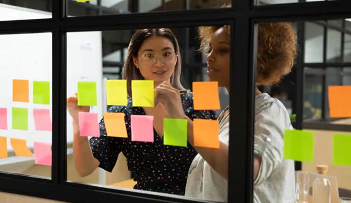 Two coworkers have a discussion at a glass whiteboard