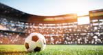 A soccer ball sits on a grass field in a stadium
