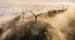 A photograph of a group of wind turbines on a misty hillside