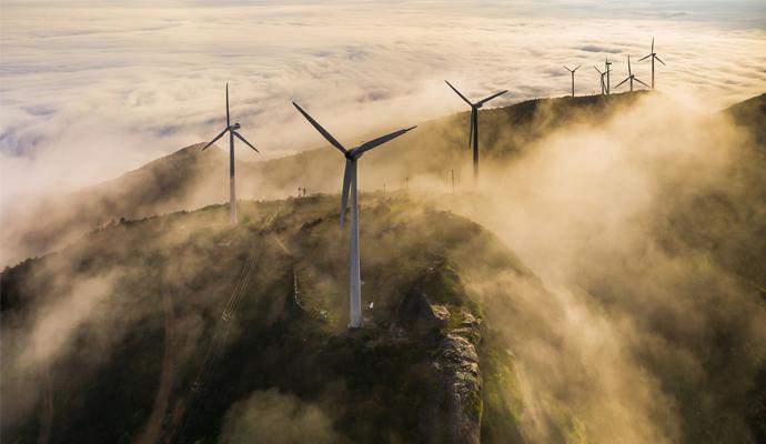 A photograph of a group of wind turbines on a misty hillside