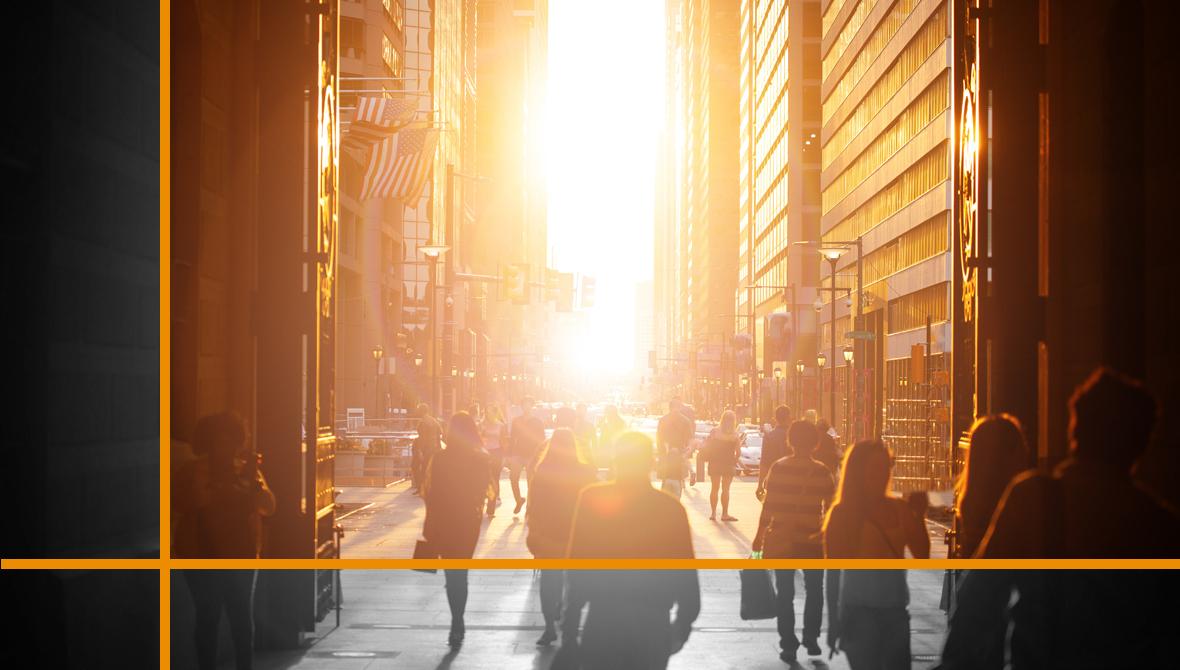 Pedestrians walk through a city street, surrounded by skyscrapers that frame the setting sun. Pedestrians walk through a city street, surrounded by skyscrapers that frame the setting sun.