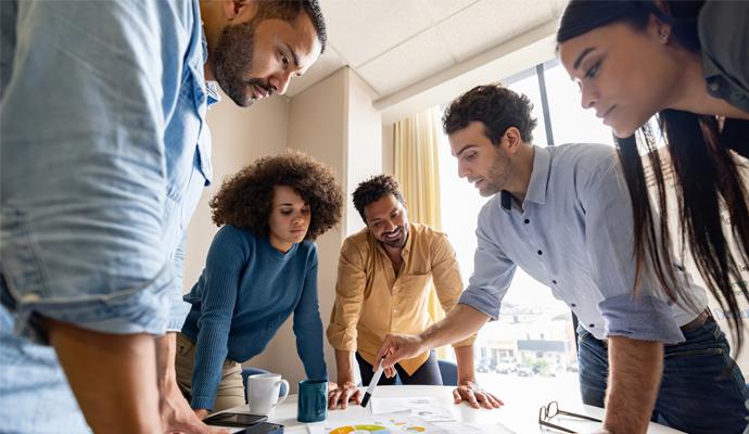 A team of colleagues gathers around a table to discuss the data in a printed report.