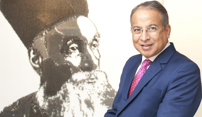 Dr. Praveer Sinha seen in a blue suit next to a pen-and-ink portrait of the founder of Tata Power, Jamsetji Tata
