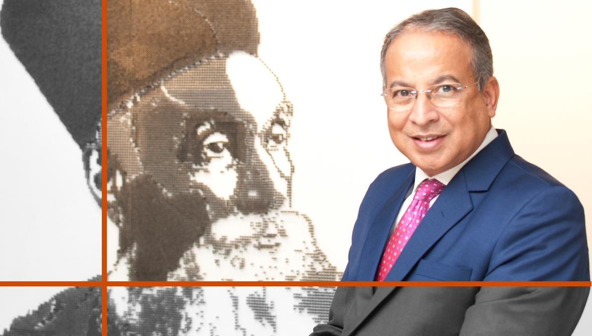 Dr. Praveer Sinha seen in a blue suit next to a pen-and-ink portrait of the founder of Tata Power, Jamsetji Tata Dr. Praveer Sinha seen in a blue suit next to a pen-and-ink portrait of the founder of Tata Power, Jamsetji Tata
