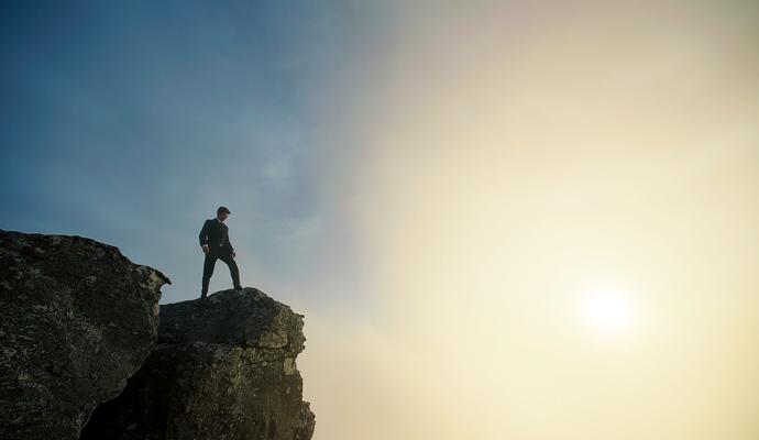 Businessman at sunset on top of a cliff with dramatic sky and clouds below