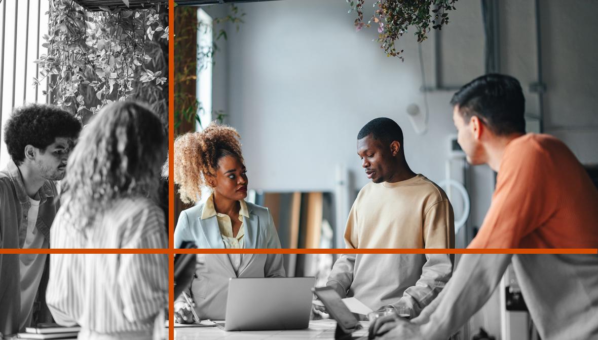A diverse group of colleagues stands and meets around a table in an informal office environment.