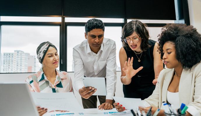 A group of four coworkers grow frustrated as they meet and talk around an office table.